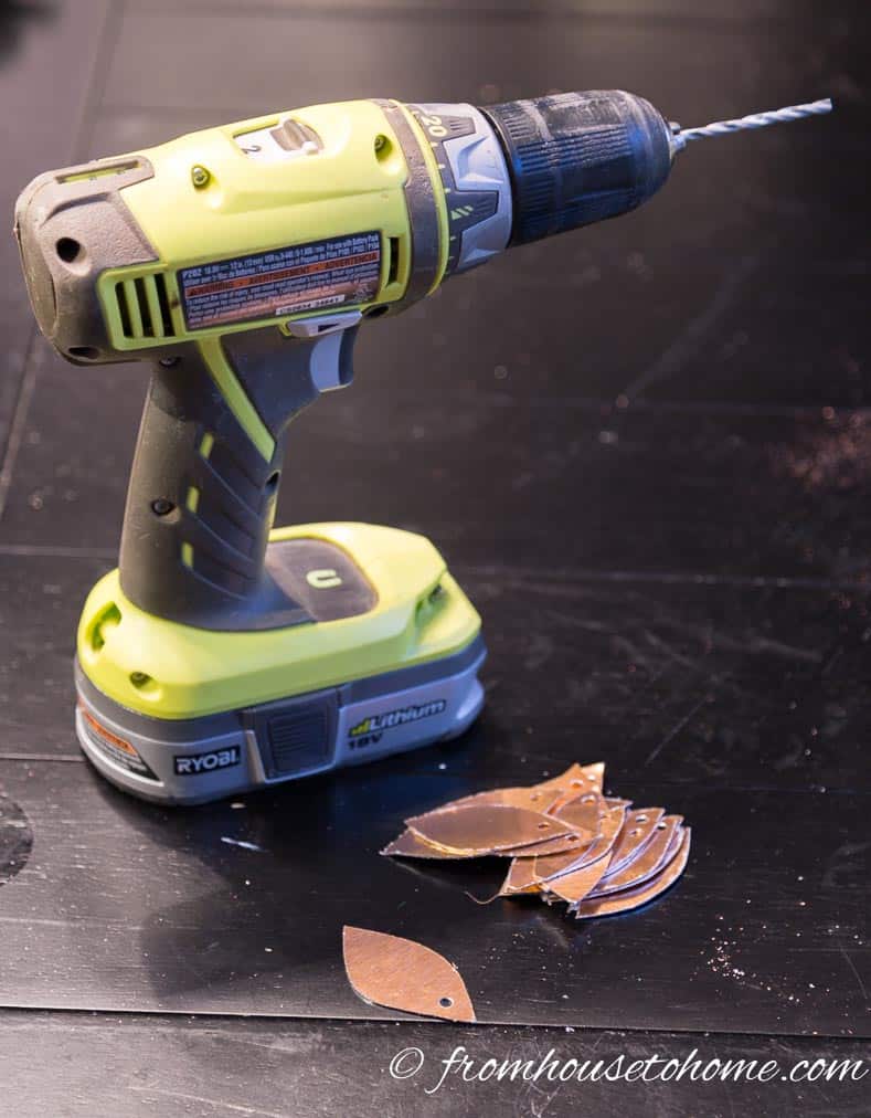 A pile of copper leaves with holes drilled in the top beside a cordless drill