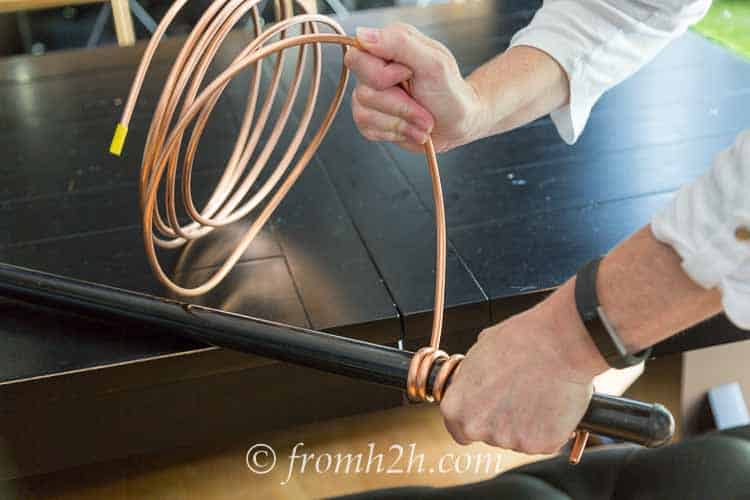 Copper tubing being wound around a broomstick handle