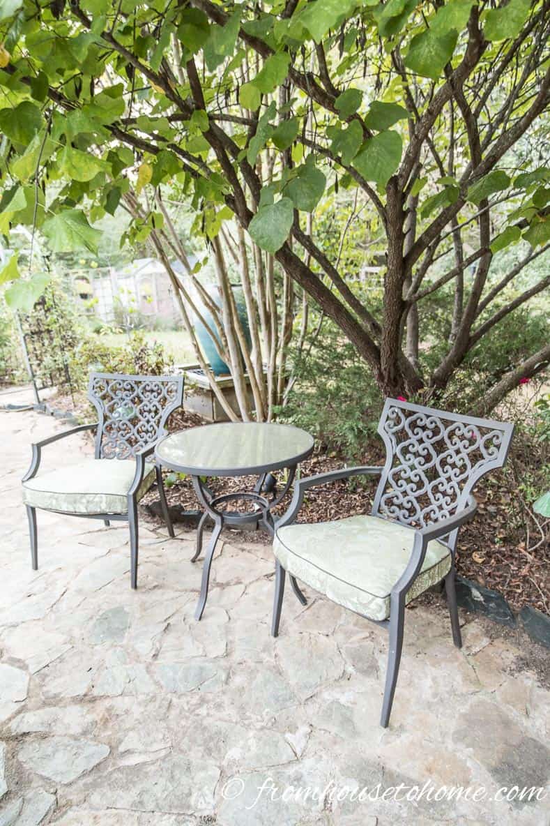 Two wrought iron chairs and a table under trees in a secret garden
