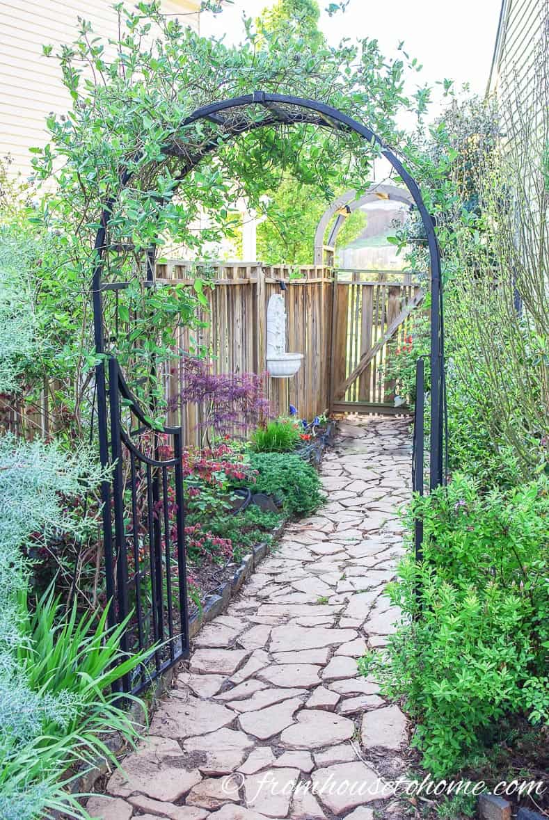 Wrought iron arbor over a side yard pathway leading into a backyard secret garden
