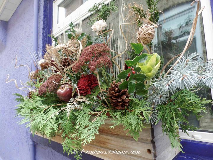 A winter window box filled with evergreens, dried flowers, pine cones and faux apple picks