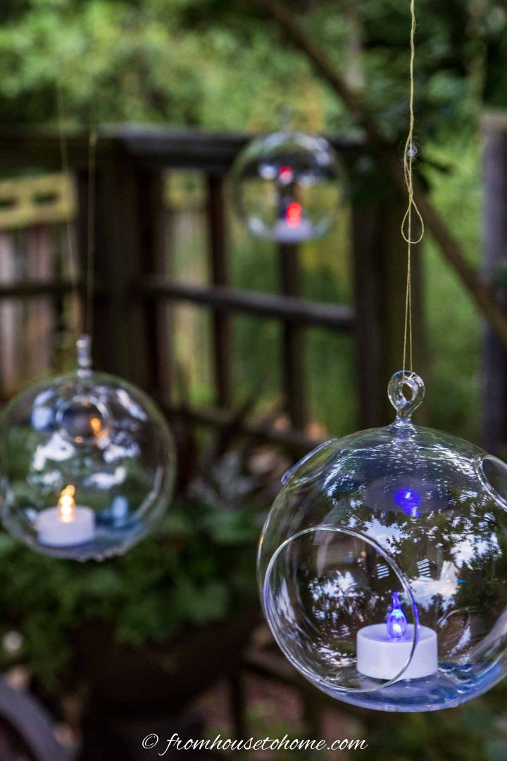 Terrarium candle holders with flame-less tealights hung from trees in the garden