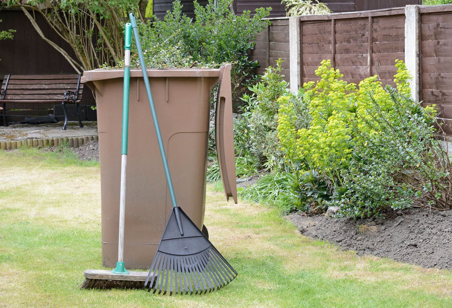 A garbage can with a rake and broom in the garden