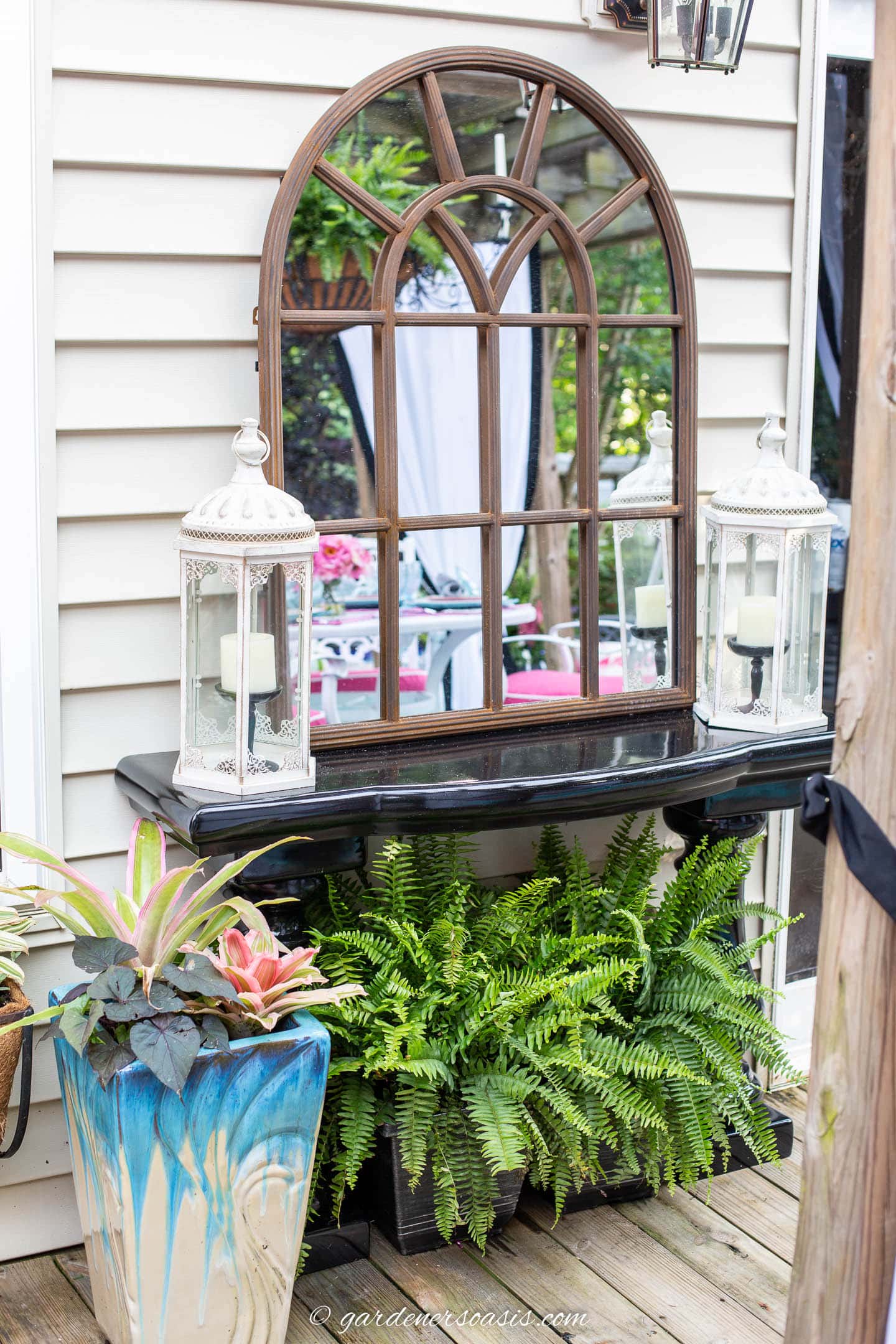 Outdoor mirror on a console table with candle lanterns and ferns on a backyard deck