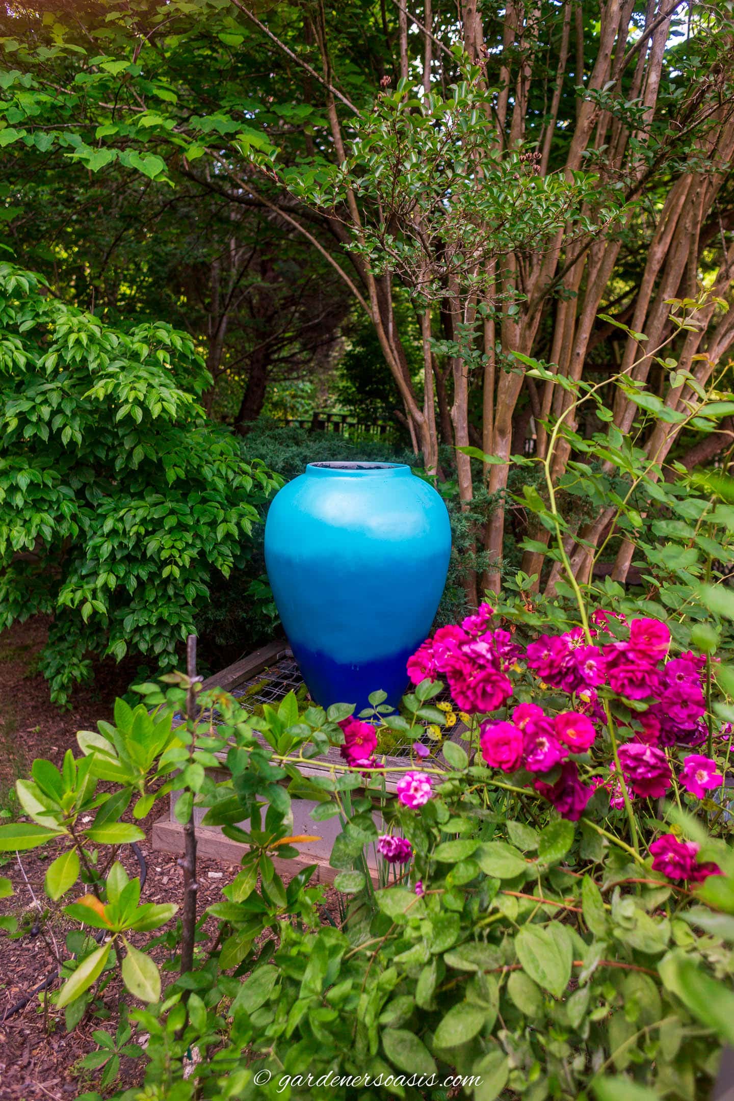 Large blue urn on a pedestal surrounded by trees and plants