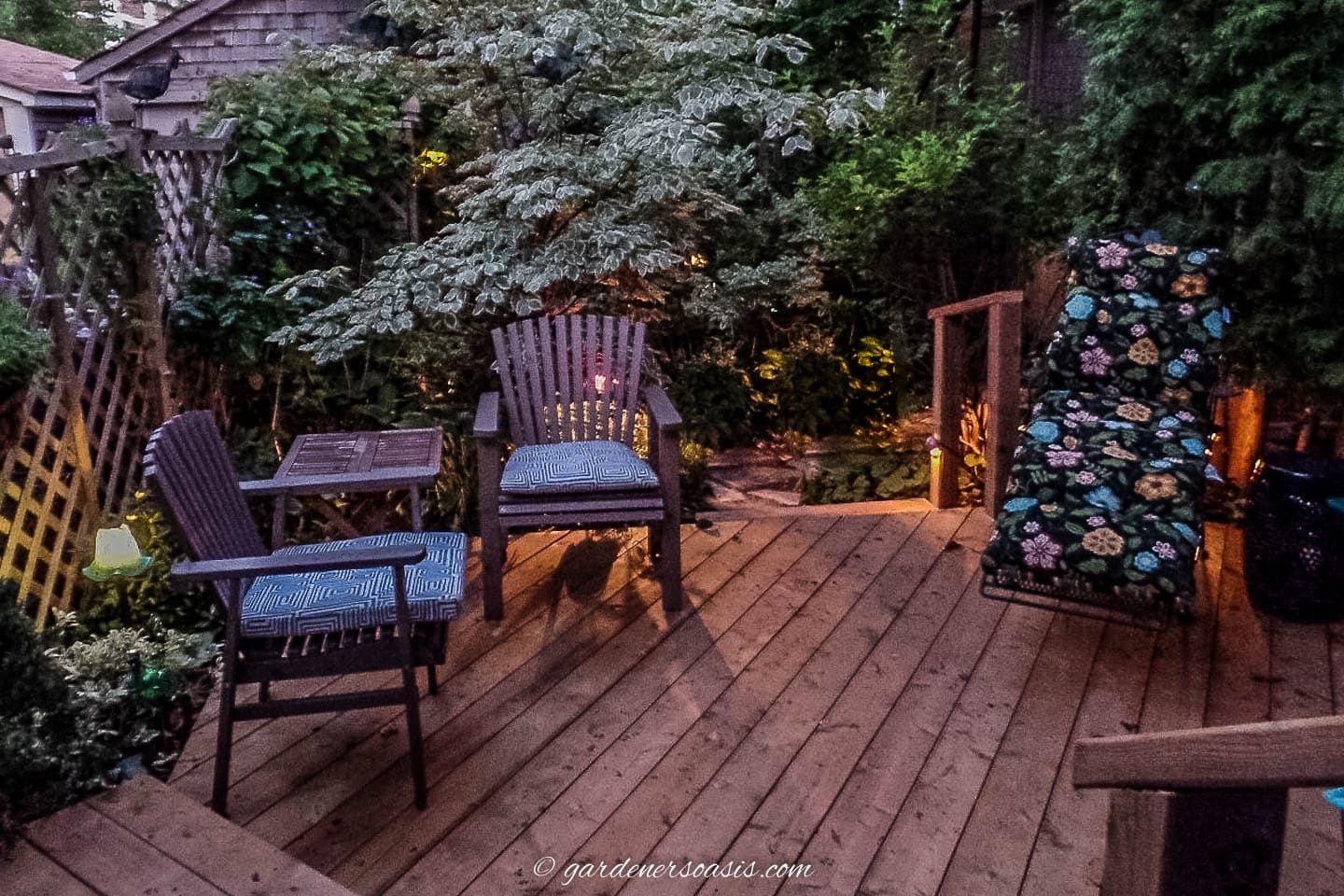 Chairs on a deck at night with landscape lights around the edge