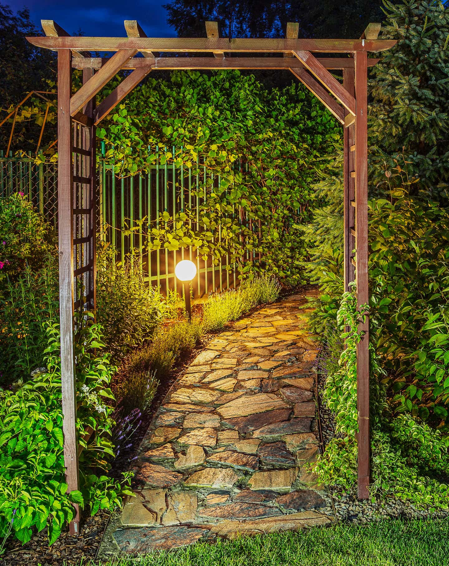 an arbor and pathway in a garden lit with landscape lights
