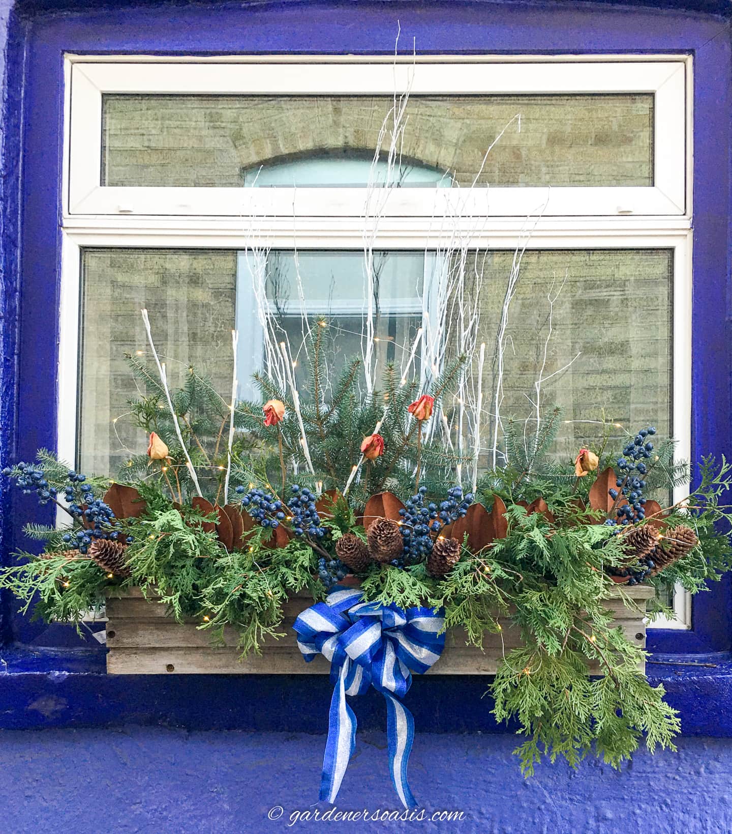 An evergreen-studded window box decorated with pine cones, berries, and a bow